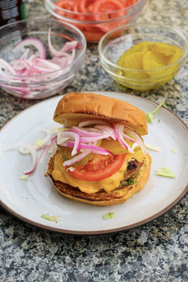 Grilled turkey burgers off the grill with pickled onions, pickles, and tomato slices as toppings
