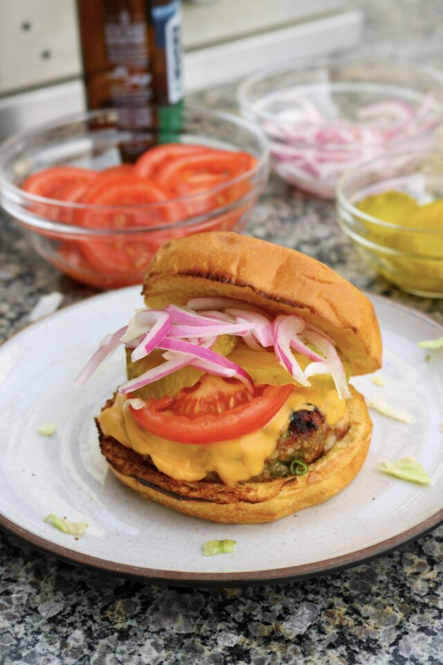 A turkey burger on a plate topped with cheese, tomatoes, pickles, and pickled onions