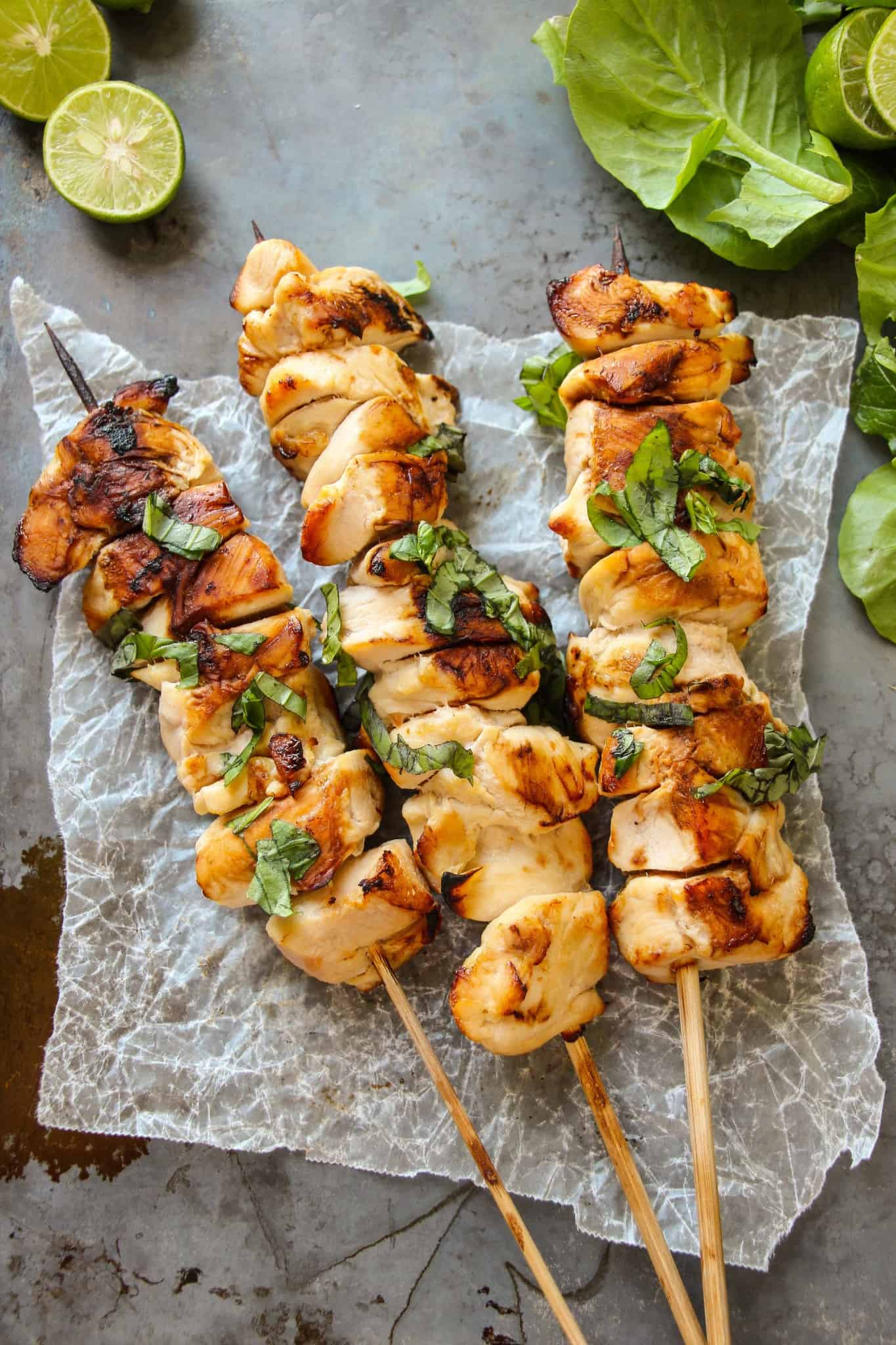 Chicken kebabs laying on a baking sheet topped with fresh basil and lime juice.