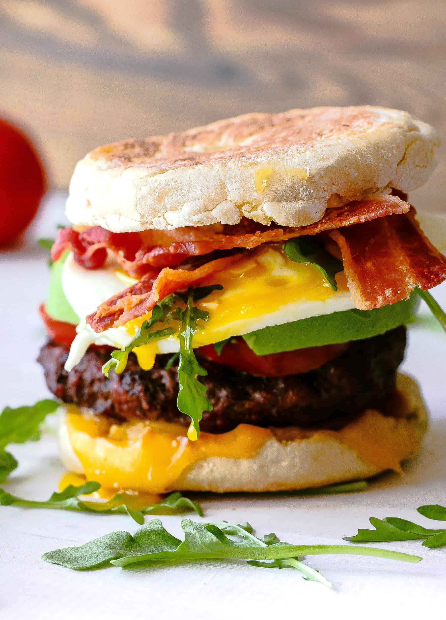 Breakfast burger plated with bacon, cheese, a burger patty, avocado, and eggs