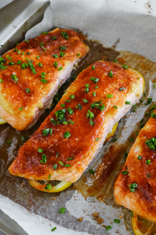 Finished blackened salmon out of the oven on a rimmed baking sheet topped with fresh chives