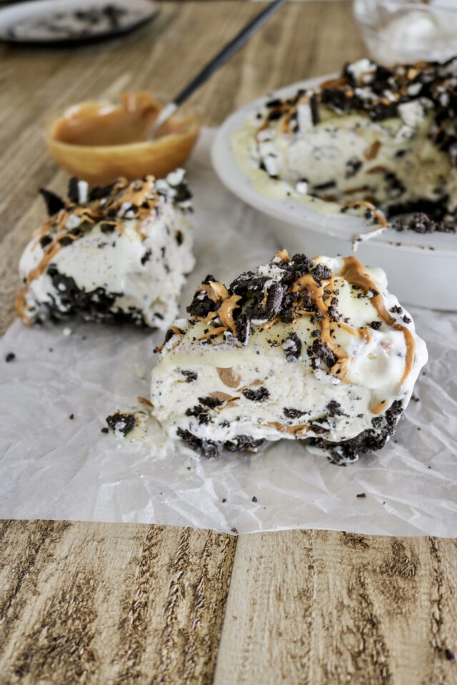 A slice of ice cream pie topped with crushed oreos and melted peanut butter