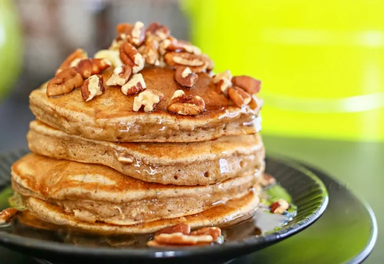 Apple butter pancakes stacked into a pile with pecans and syrup drizzled over top