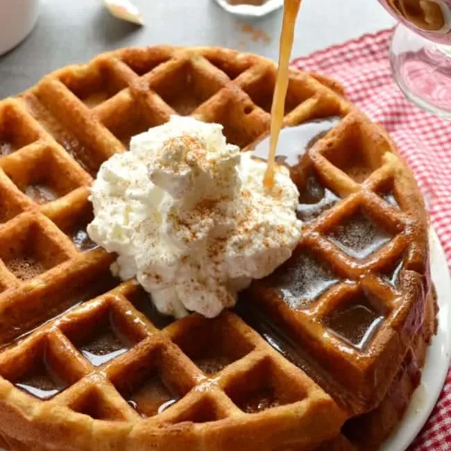 Plated waffles with whipped cream and cinnamon syrup being poured over top