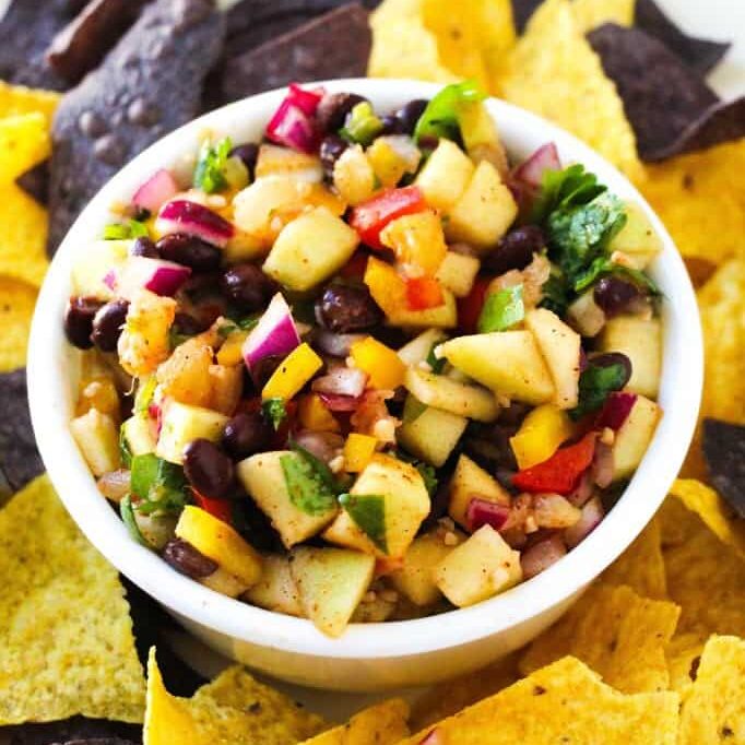Apple salsa in a small bowl surrounded by tortilla chips