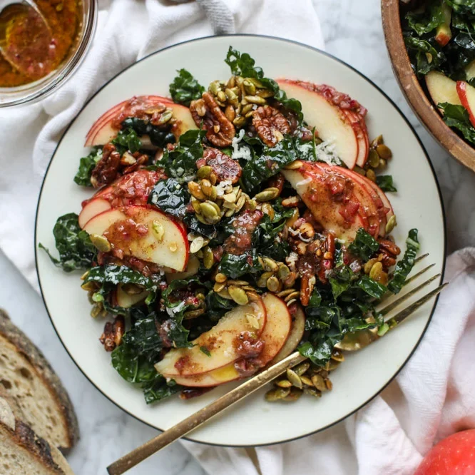 A kale salad with nuts and apples on top plated with a fork