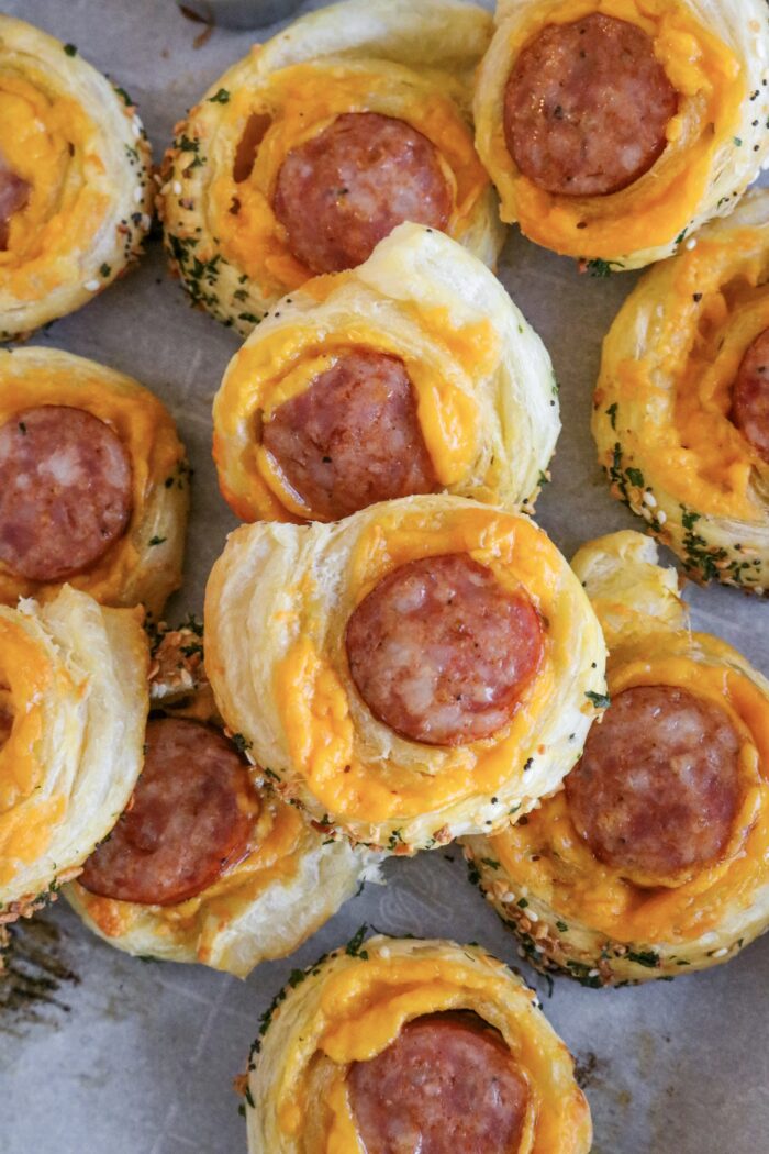 Finished Sausage rolls with puff pastry piled on a baking sheet