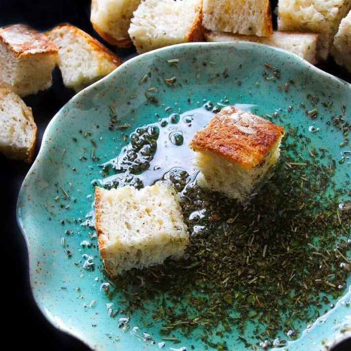 A serving dish with bread oil in it and couple bread pieces in the oil